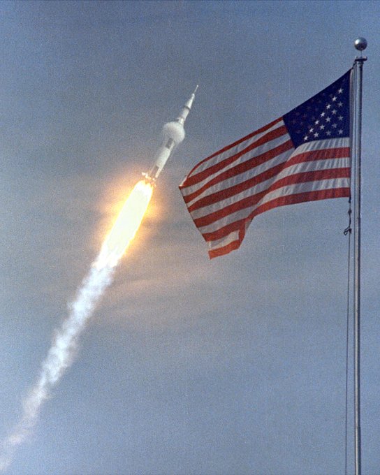 Saturn V rocket launch with American Flag in foreground.