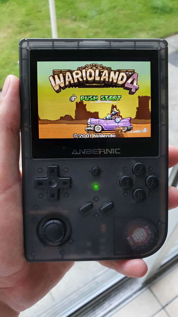 A hand holding an Anbernic RG351 running Warioland 4.