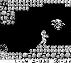A screenshot from Metroid 2. Samus is in a tunnel, getting ready to shoot missiles at an Alpha Metroid. An empty husk is on the ground to the left.
