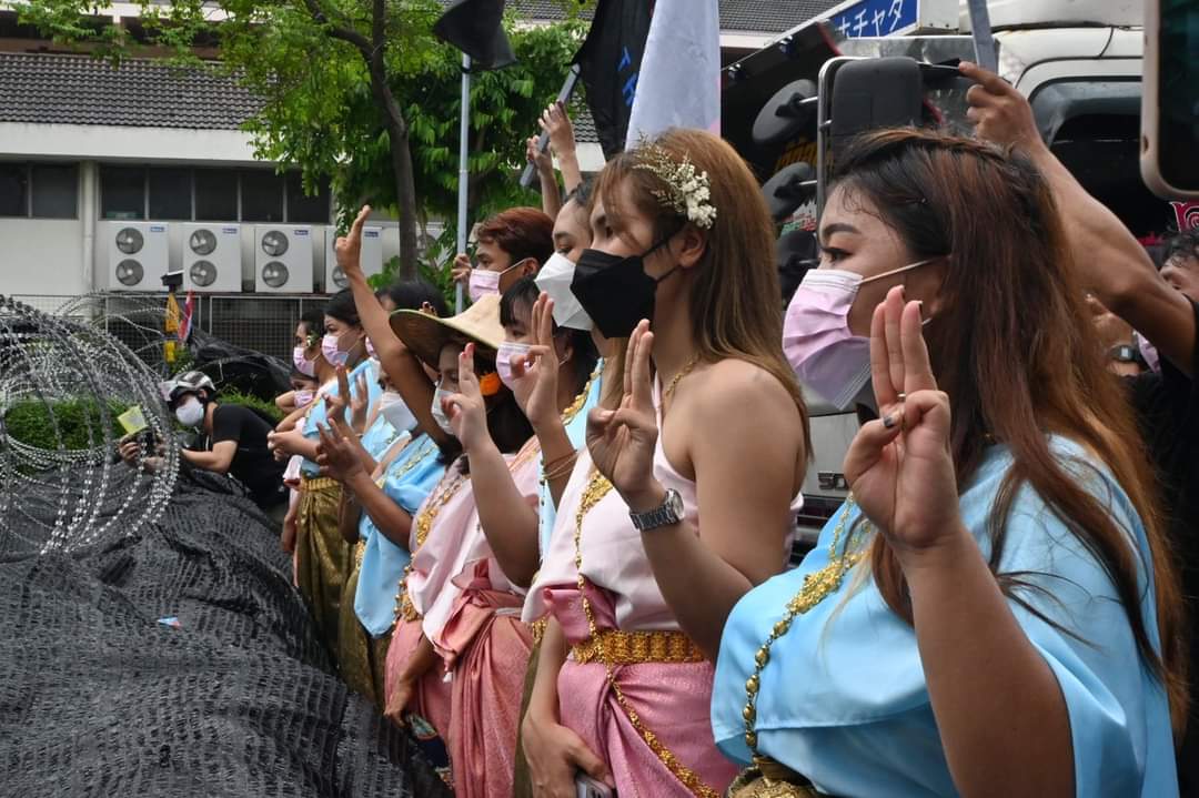 Protesters dressed in traditional Thai costumes hold up three fingers near Government House. #ม็อบ25กรกฎา