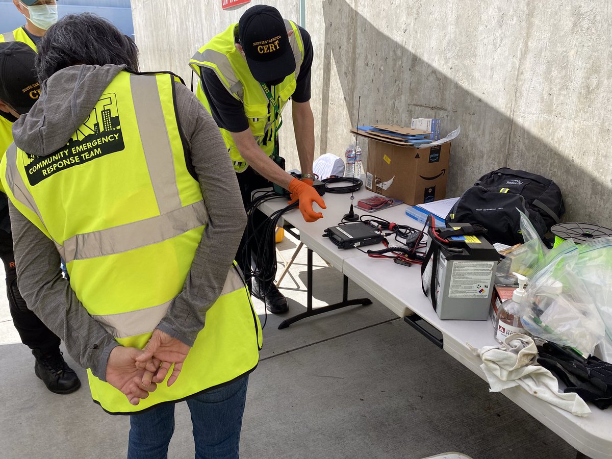 CERT volunteers gathered outdoors under a canopy, discussing the use of radio equipment.