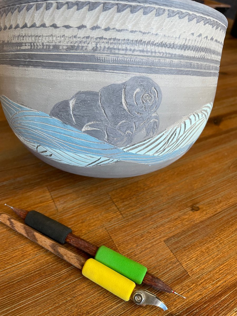 A second tardigrade emerging majestically from behind the stylized water on the same pot. Carving tools in the foreground.  