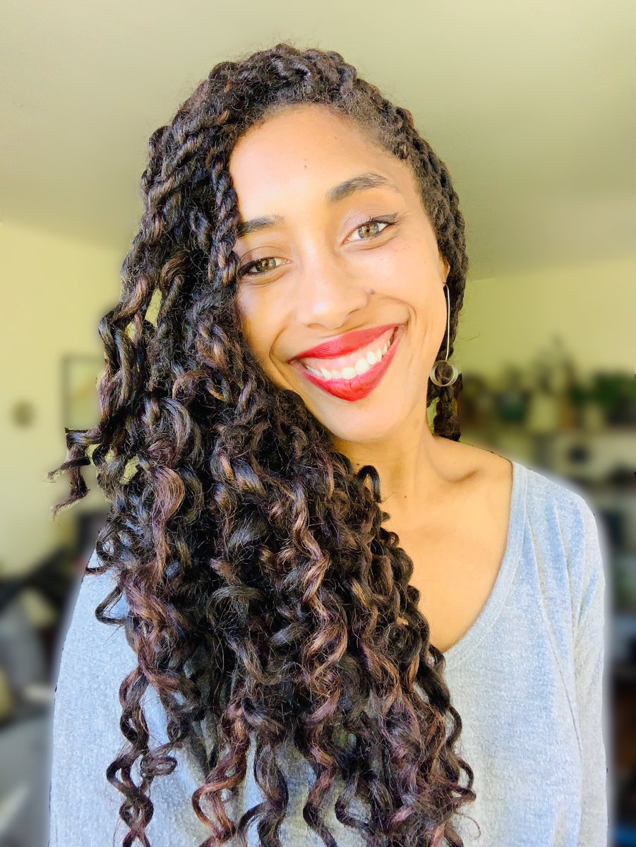 Brielle is pictured in her living room, directly facing the camera, smiling wide.