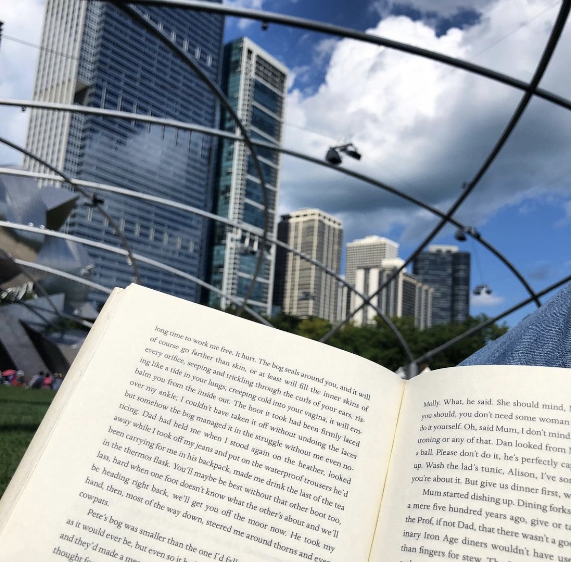 A blue sky with clouds sits above tall buildings and a metal pipe pavilion in Millennium Park. An open book is in the foreground with text on both pages.