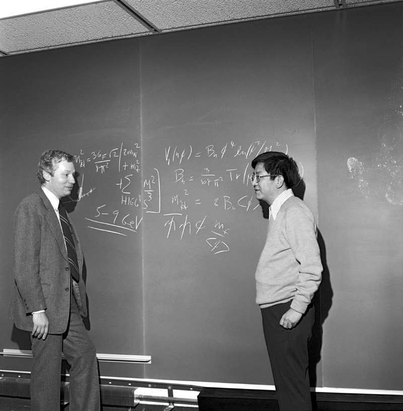Weinberg and Lee standing in front of a blackboard with equations written on it.