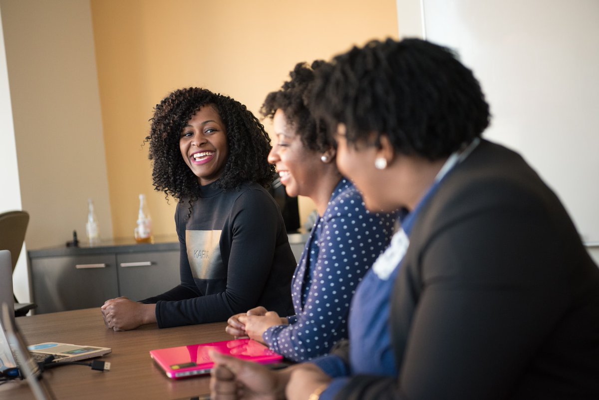 a smiling woman at a desk looking at two other woman next to her also smiling at her