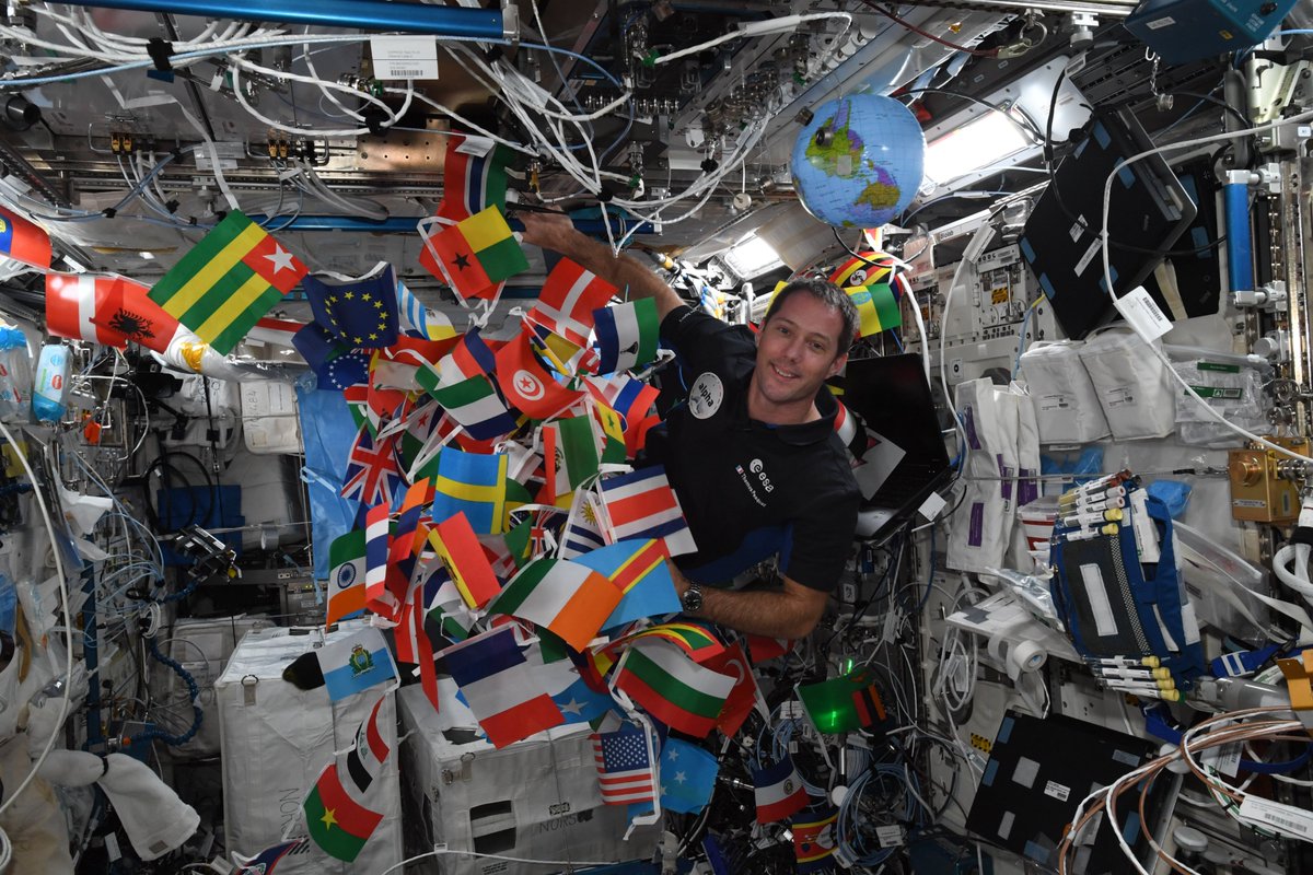 Thom_astro's tweet photo. J'avais emporté un petit drapeau de chaque pays du monde dans ma valise : maintenant ils ont tous volé dans l'espace 😊 Par contre le rangement a été un peu délicat : les cordes ici, c’est pire que les câbles d'écouteurs sur Terre - Shane et Mark ont dû venir à ma rescousse 😅 https://t.co/m2p2aImX6E