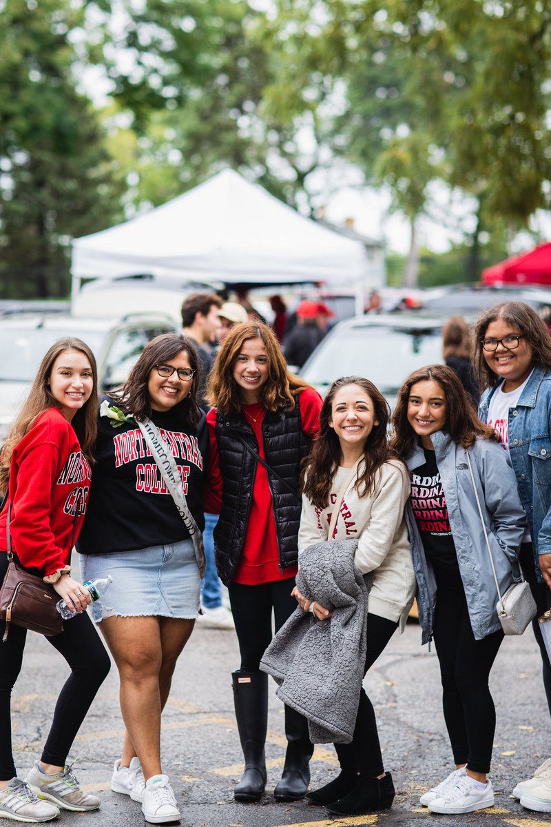 A photo of six North Central College students at a football game. They are all wearing North Central gear and are smiling at the camera. 