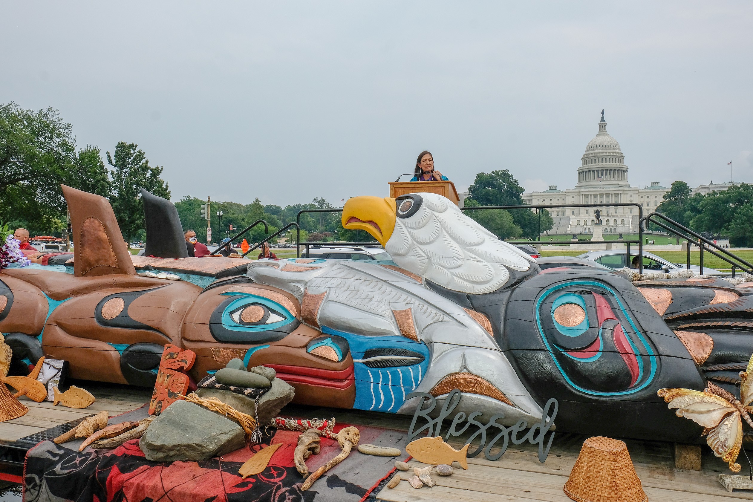 Secretary Haaland stands in front of the US Capitol Building with the totem in the foreground.