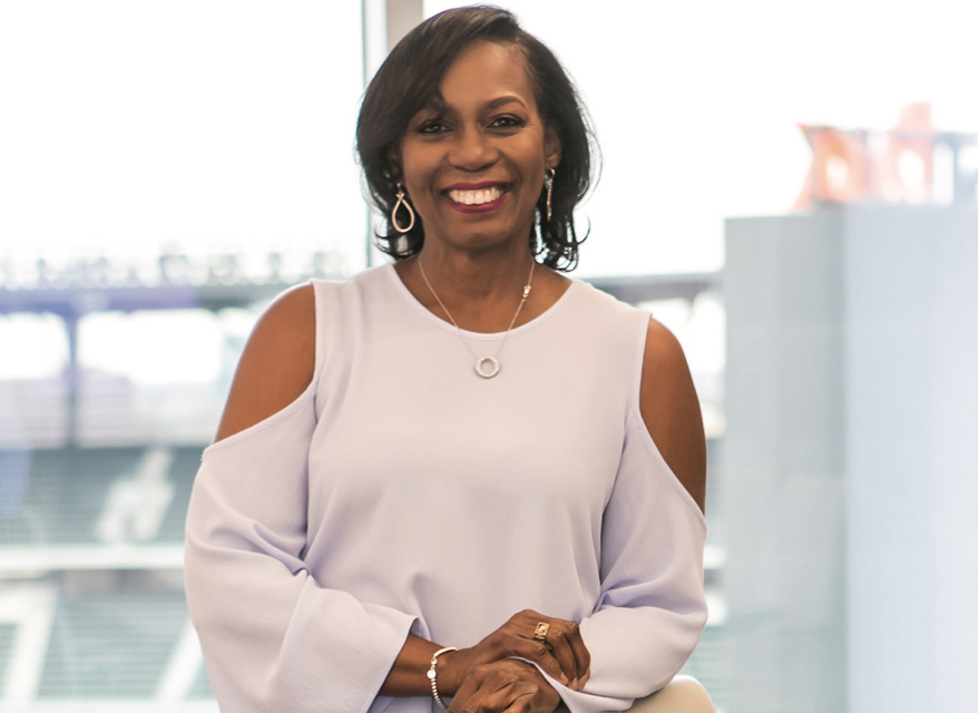 Burunda Prince is standing in front of a window. There are industrial silos behind her. She smiling brightly.