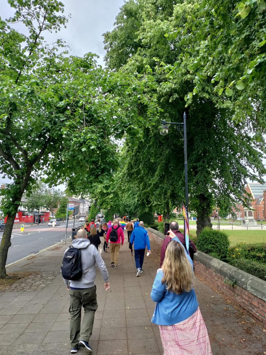 Image shows students and staff walking with Pride flags in front of Queen's University Belfast.
