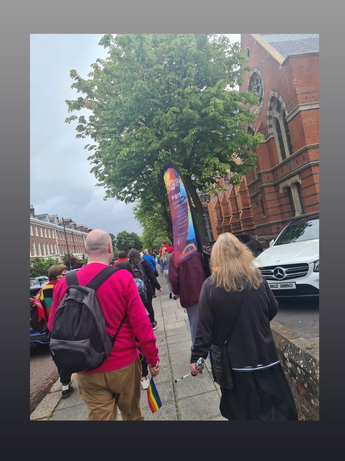 Image shows students and staff walking with Pride flags beside Queen's University Belfast.