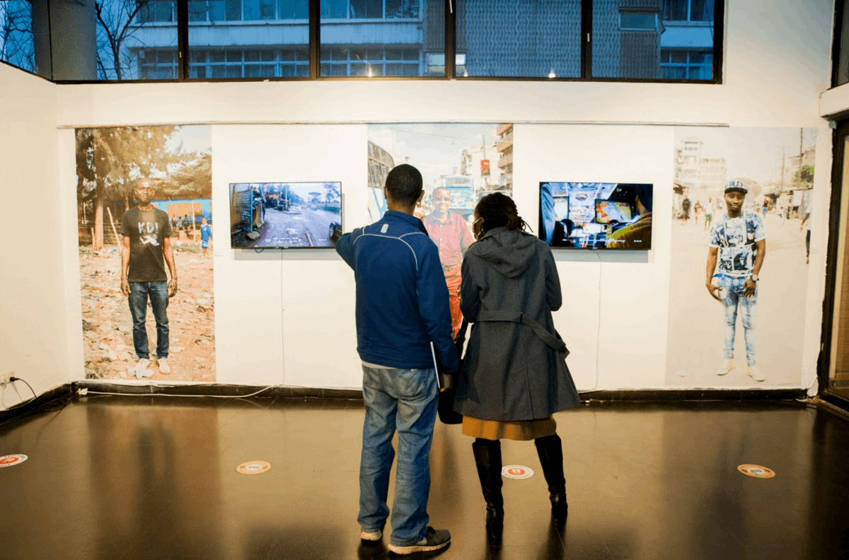 Two visitors at the exhibition, they are looking at three of the four individuals whose experiences are highlighted.