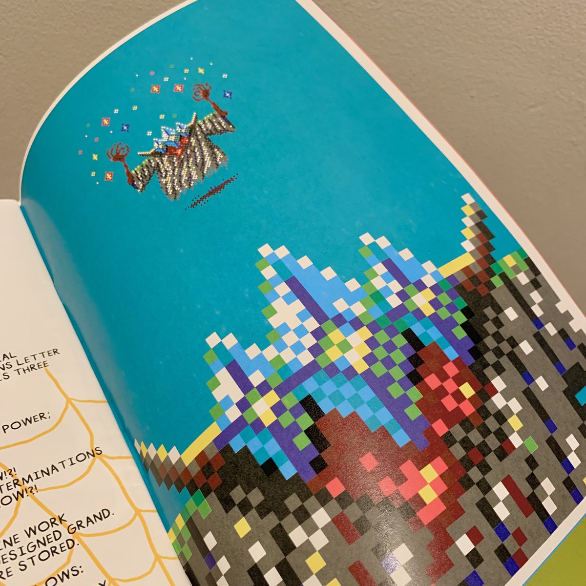 Photo of an open book showing the Floating Pixel Witch artwork. The artwork is reproduced at a small size at the top of the page, and a cropped close-up appears at the bottom, showing the pixels up close.