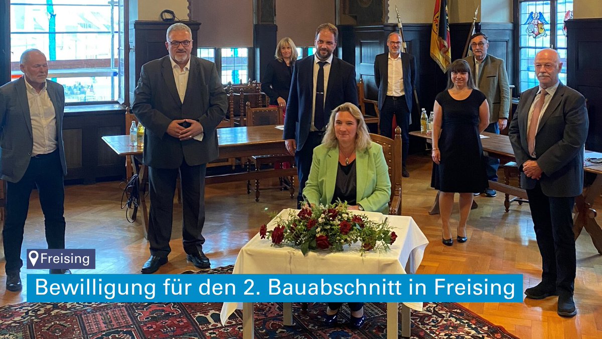 Mehrere Personen in einem Sall, darunter Bauministerin Kerstin Schreyer an einem Tisch mit Blumenschtrauß; Text: Bewilligung für den 2. Bauabschnitt in Freising