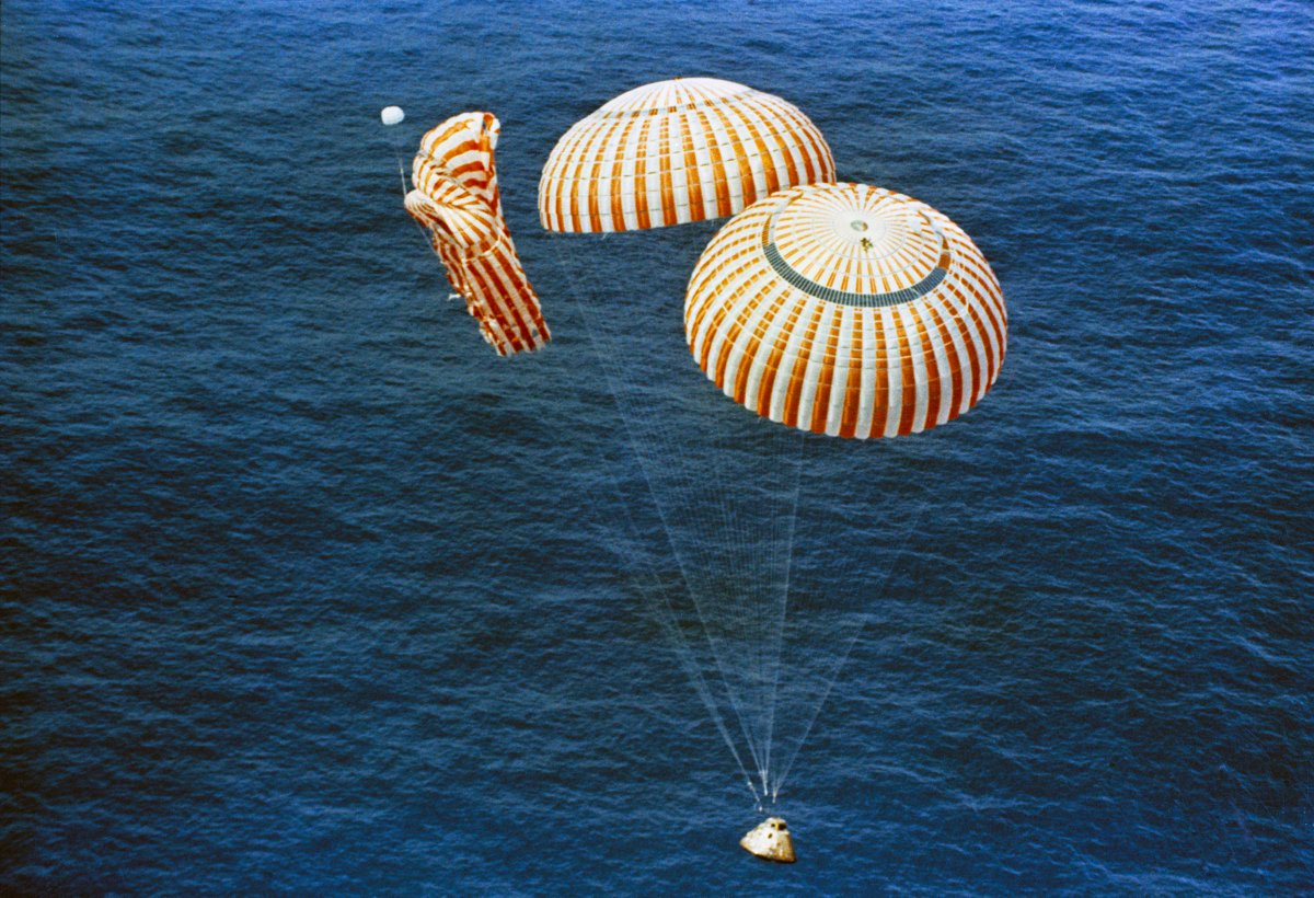 Command module about to splashdown in the ocean with two of the three white and red parachute deployed