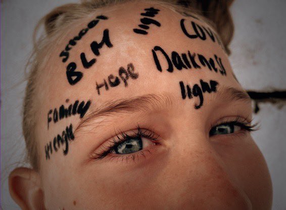 Close up of girl’s face with words written across her forehead.