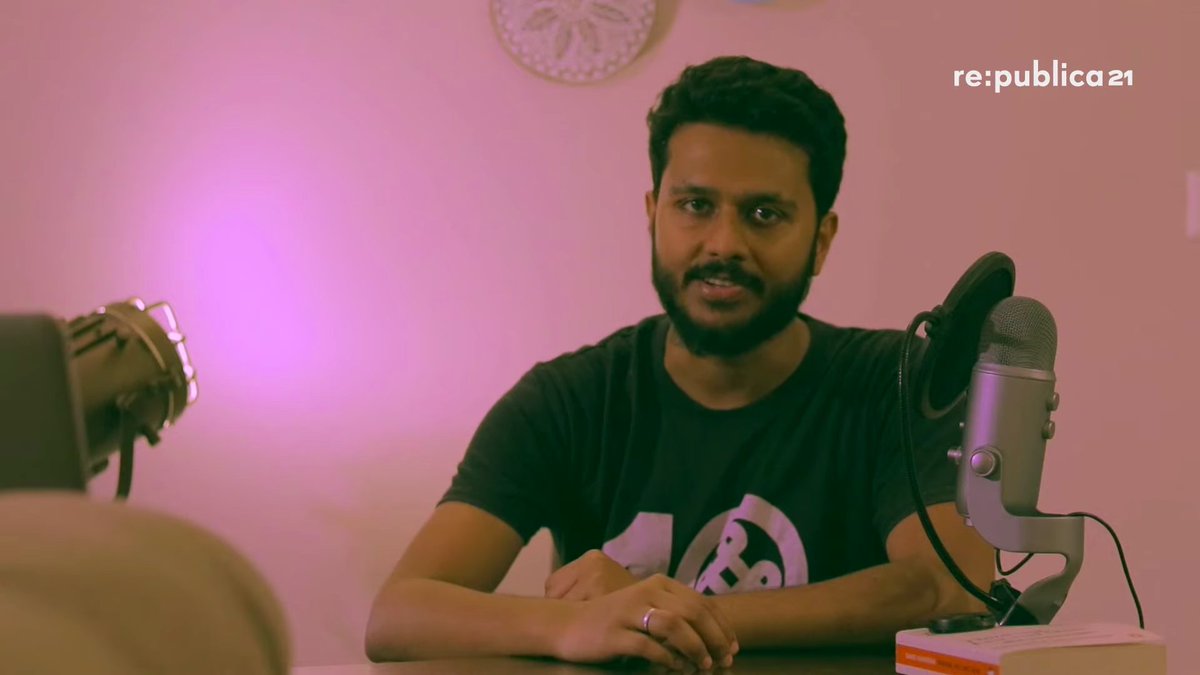 Subhashish Panigrahi an einem Schreibtisch mit Mikrofon vor einer rosa beleuchteten Wand. Screenshot aus seinem rp21-Talk „No Digital Rights if You Are Marginalized in India“.