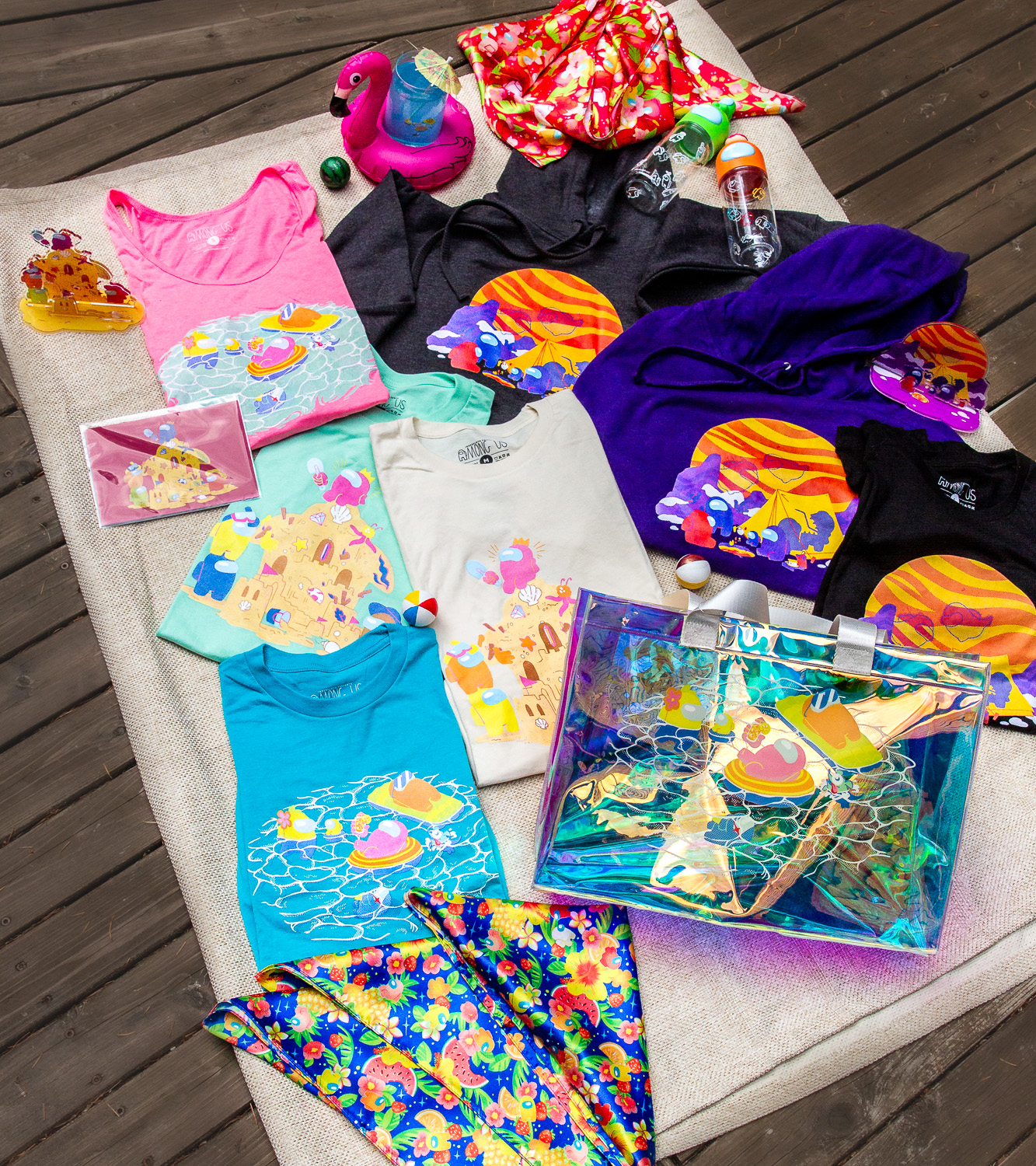 A flat lay of various merchandise, including summer themed shirts, hoodies, tank tops, headscarves, acryllic stands, a holo tote bag, and water bottles.