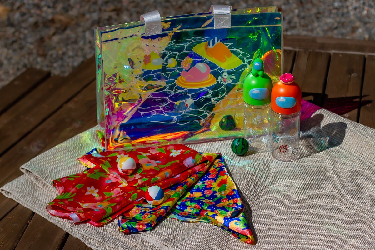 A product shot of the holo tote bag, headscarves, and water bottles. Surrounded by tiny beahc balls and watermelon decorations. 