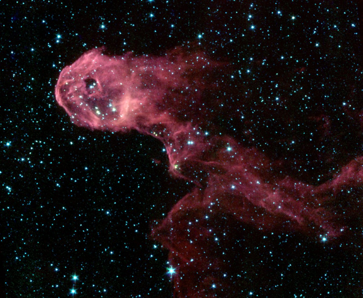 The Elephant's Trunk Nebula, as imaged by the Spitzer Space Telescope, resembles a reddish concentrated ball of gas (left) connected to a long tail flowing behind it. Tiny dots as stars are seen in the background.