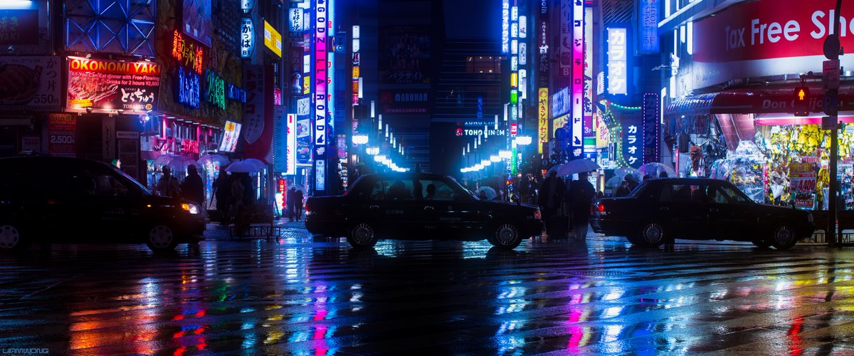 Tokyo at night. Shinjuku in the rain. A taxi is at the centre of the frame. Reflections from the neon signs light up the scene.