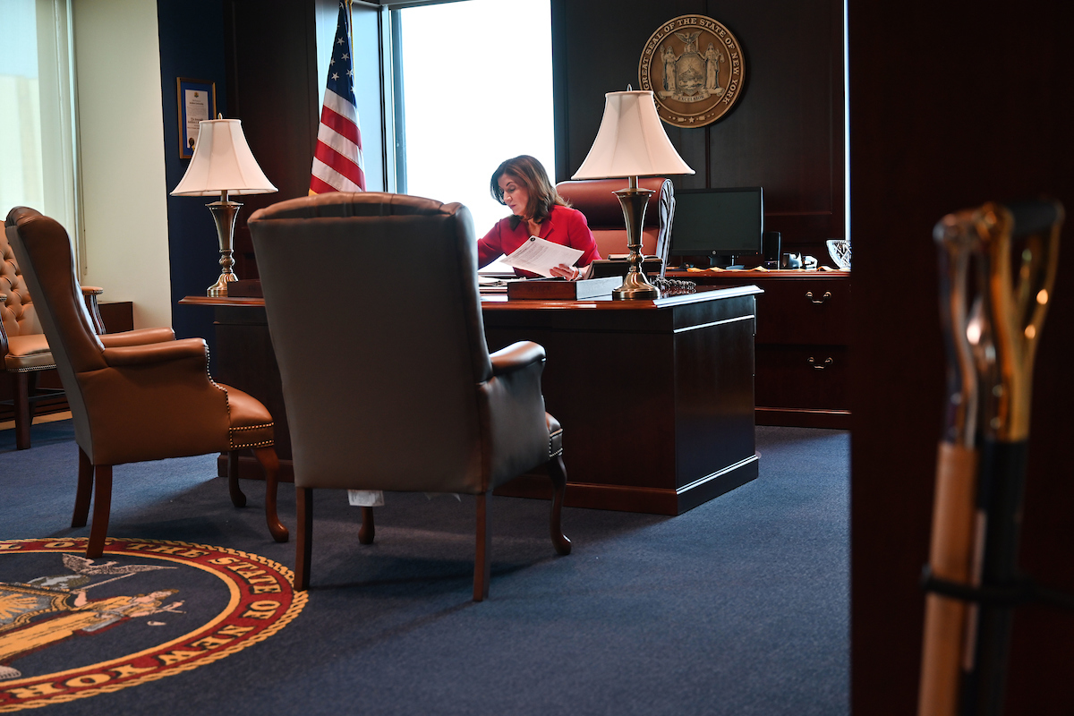 Governor Hochul sits alone at desk in office with papers in hand