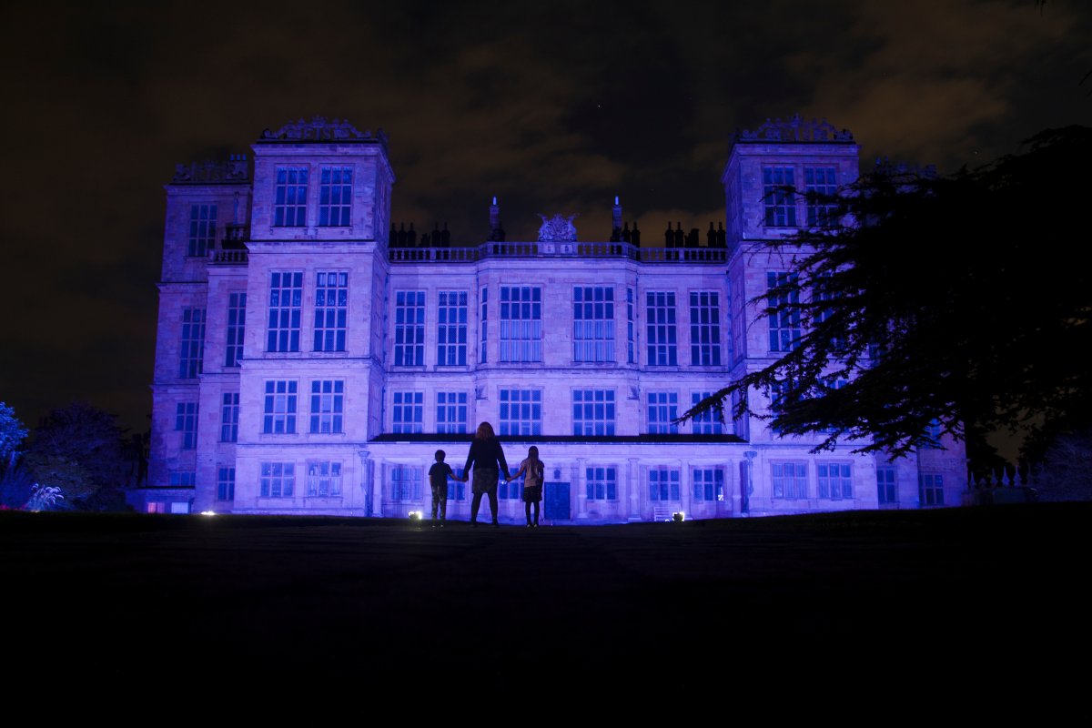 Silhouette of an adult and two children standing in front of the Elizabethan house at Hardwick which has been illuminated with purple light