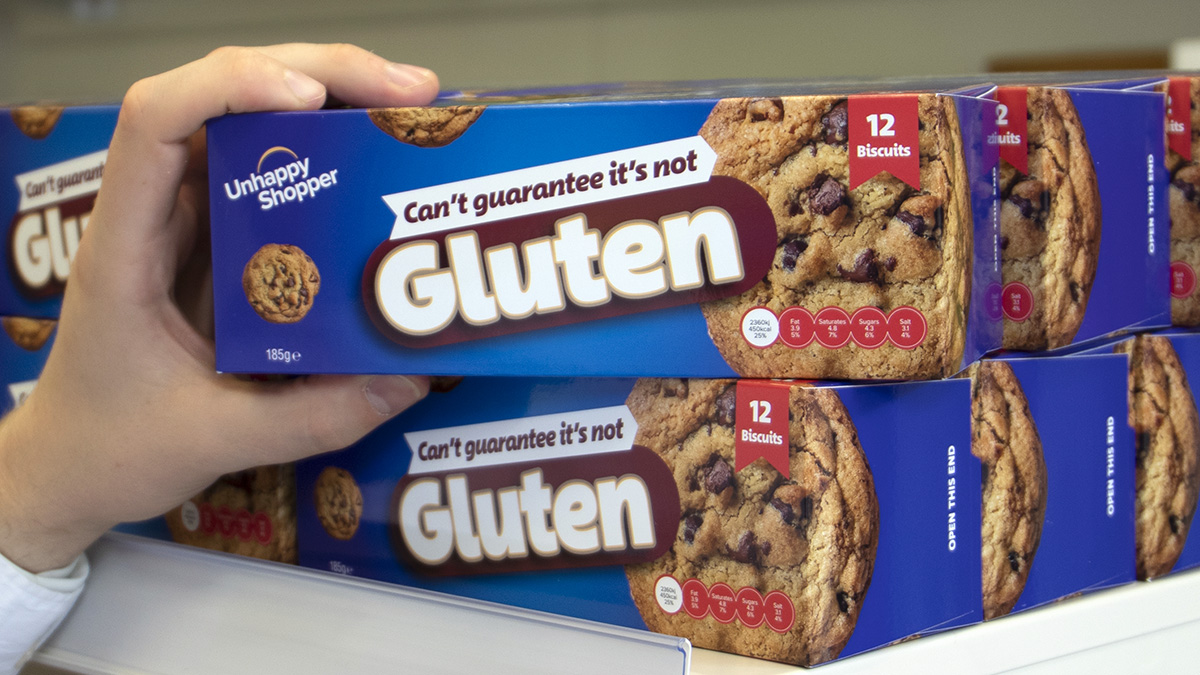 A hand picking a box of biscuits off a shelf. The name of the biscuits is Can's guarantee it's not gluten and the brand is Unhappy Shopper.
