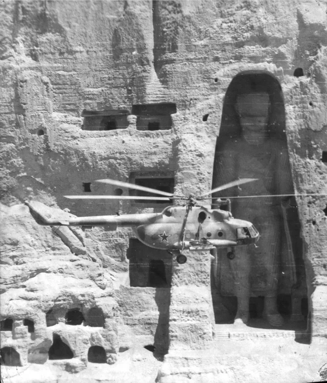 Historybench's tweet image. A Soviet Mi-8 helicopter flying past one of the two Buddhas of Bamiyan, Afghanistan 1980