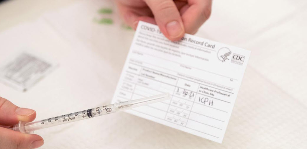 Hands holding a vaccination card and a needle.