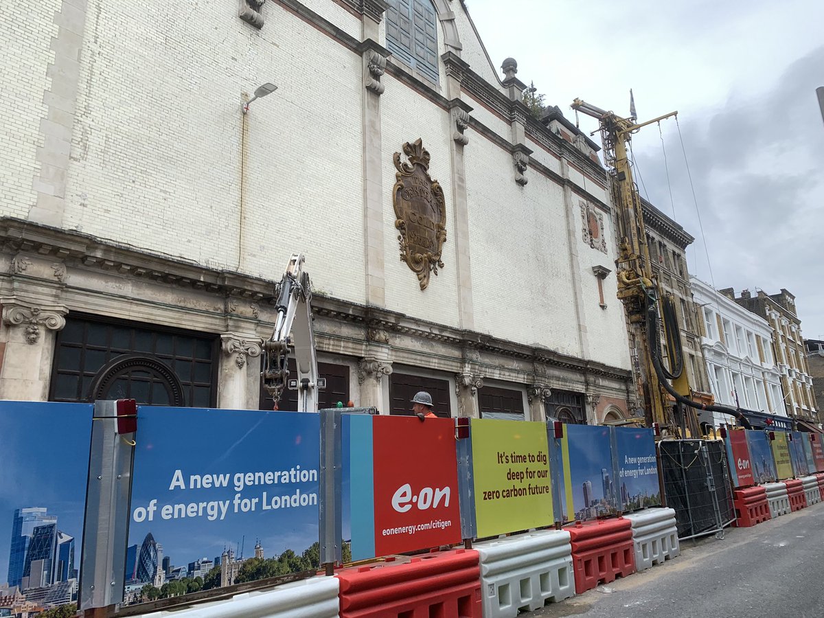 E-ON branded hoardings on a street by Farringdon. Text on signs say “a new generation of energy for London” and “it’s time to dig deep for a zero carbon future” an old crest on the building behind says “central cold storage”