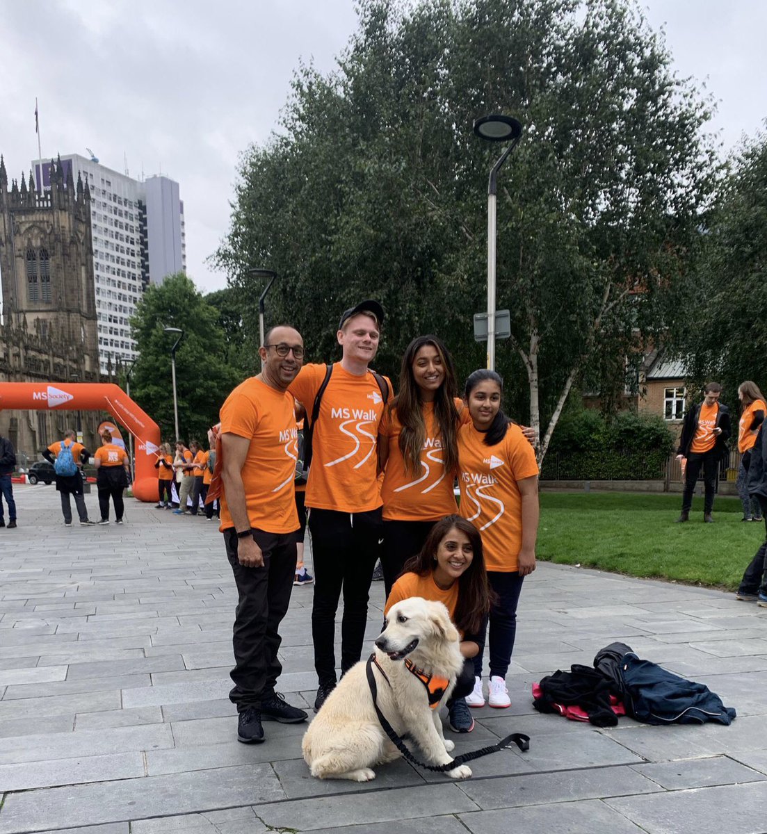 MS Walk in Manchester. Friends and family posing for a photo before they start their walk. They have their dog with them who is also wearing an MS Walk T-Shirt.
