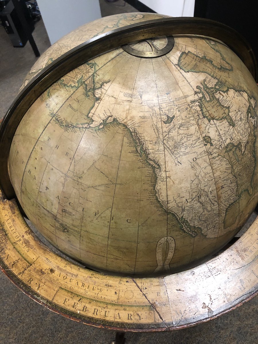 A worn globe showing western north america and the pacific in an elaborate stand with astrological info