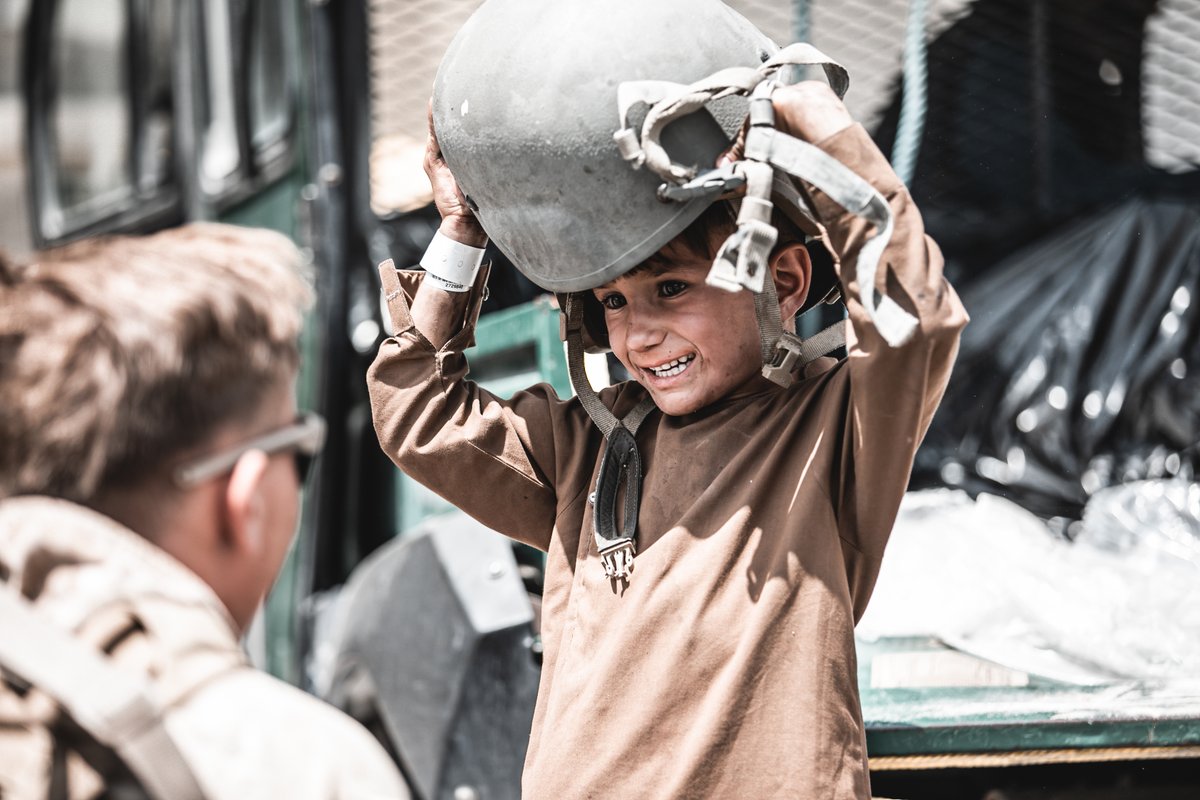 A U.S. Marine assigned to Special Purpose Marine Air-Ground Task Force – Crisis Response – Central Command hands a helmet to a child awaiting evacuation at Hamid Karzai International Airport, Afghanistan, Aug. 22, 2021. The U.S. is assisting the Department of State with a Non-Combatant Evacuation Operation (NEO) in Afghanistan. (U.S. Marine Corps photo by Gunnery Sgt. Melissa Marnell).