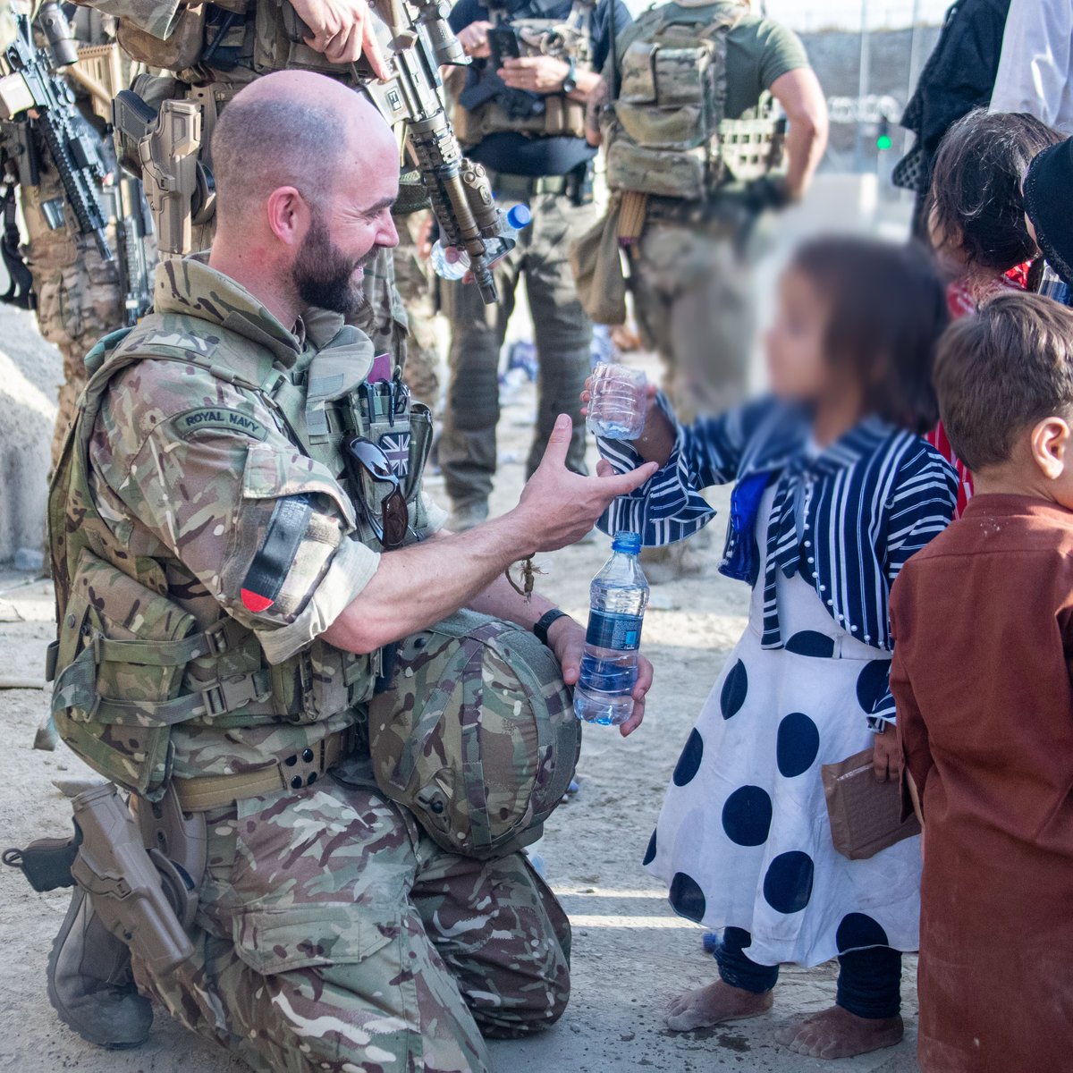 Member of the UK Armed Forces offering water to a child.