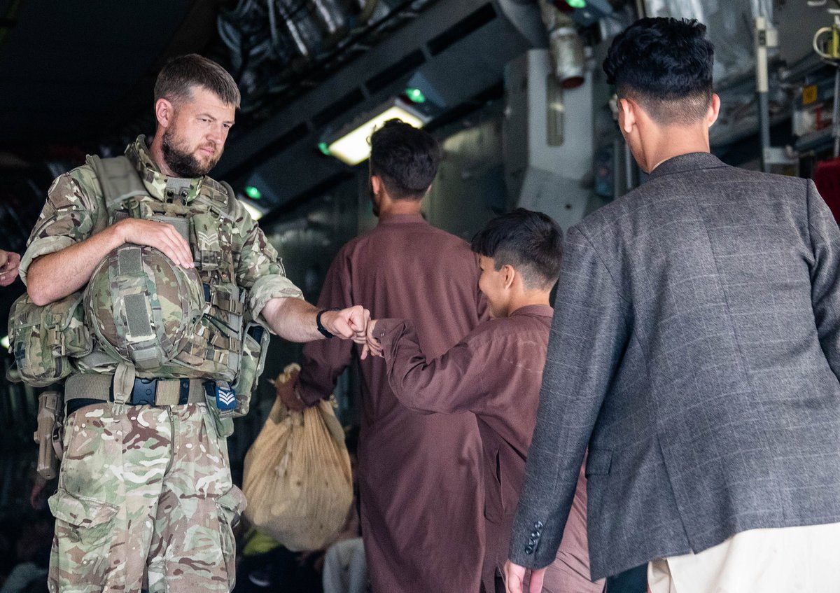 Member of the UK Armed Forces welcoming a child onto a plane.