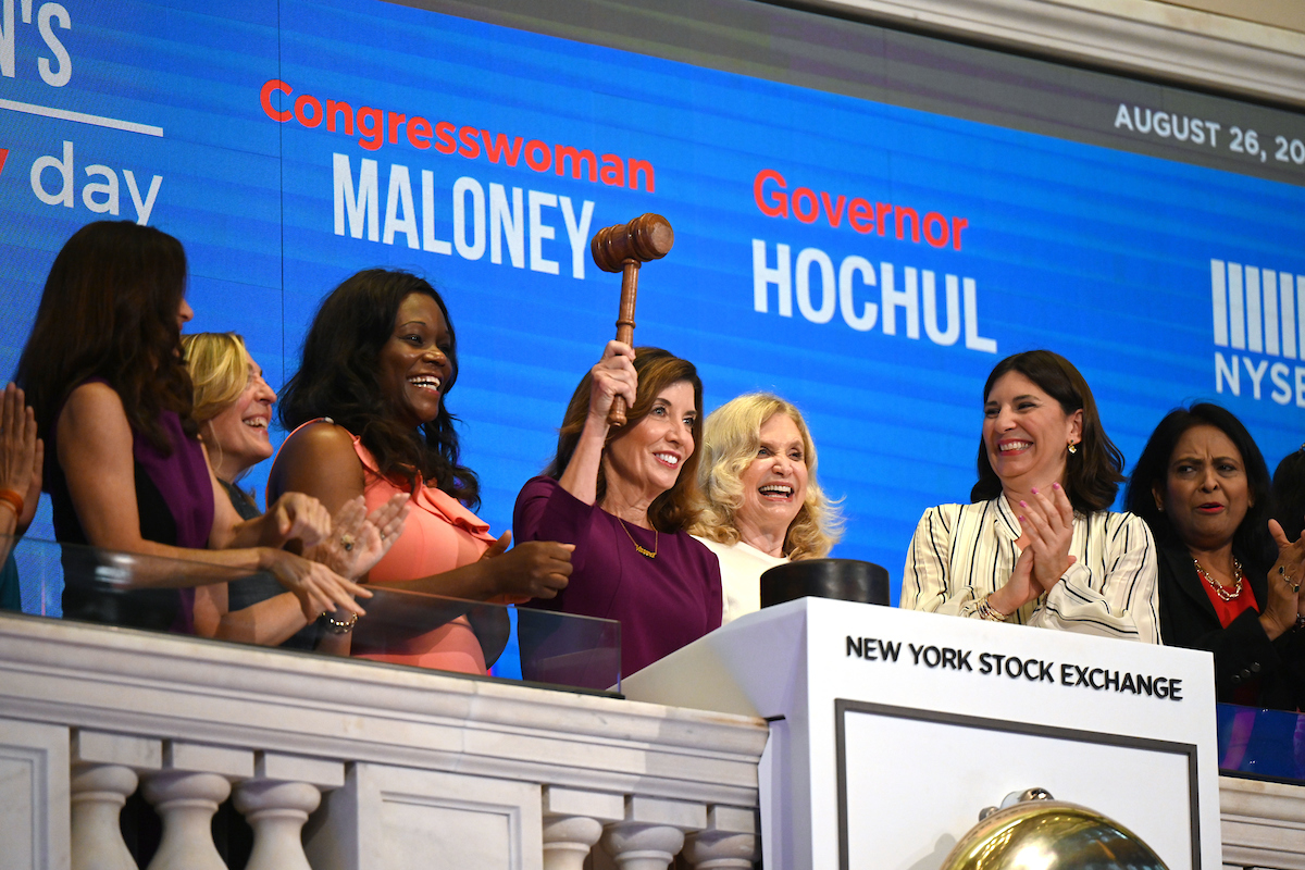Governor Hochul (center) rings the closing bell at the New York Stock Exchange with Congresswoman Carolyn Maloney (immediate right) and surrounded by other women clapping.