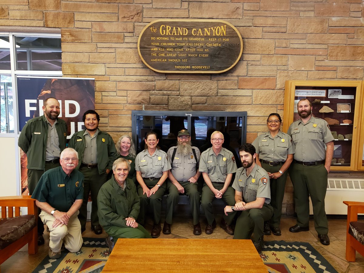 A group of uniformed park rangers sitting in front of a fireplace in park headquarters.