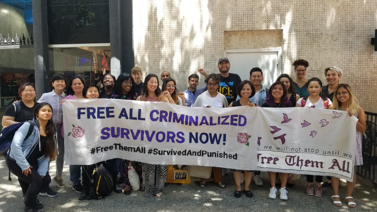 Group photo of 20 people behind banners that read "free all criminalized survivors now! #FreeThemAll #SurvivedAndPunished" and "we will not stop until we free them all" with Rose's and flock of birds flying away