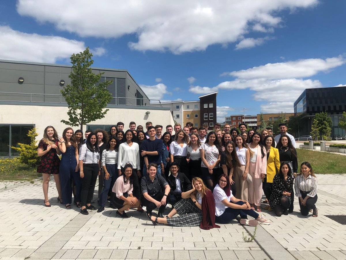 Photograph of the current year of Microsoft interns working at the Microsoft UK offices. The sky is blue with clouds and there are trees in the background.