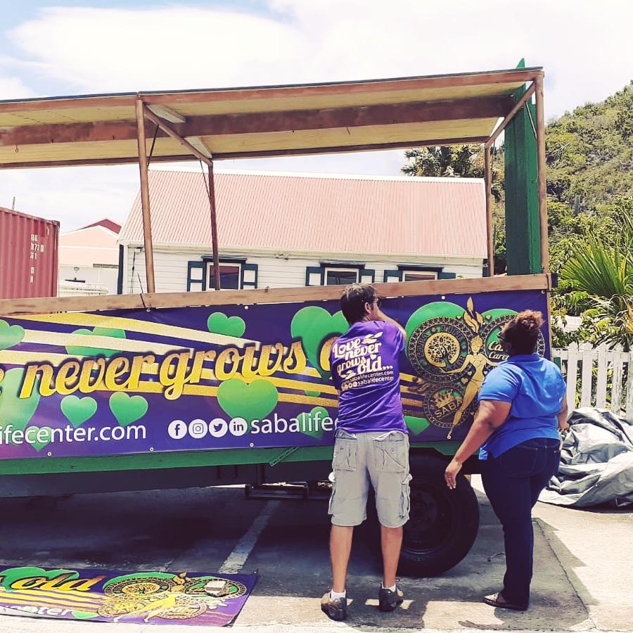 SabaLifeCenter's tweet photo. The banners are up! Getting ready for the road! Saba Carnival here we come!

Staff from @HomeOfSaba &amp; @SabaHealthCare together with @mal2m putting the banners in place.

Love Never Grows Old 💚💛💜

#SabaLIFE #carnival #Saba #Caribbean #EndLoneliness #seniorcare #ikzorg https://t.co/BF9hc8DDKH