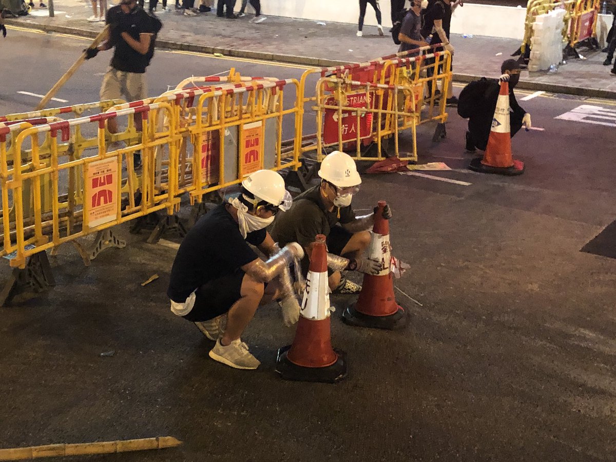 THREAD: How do HK’s  #HardHatRevolution protesters neutralize police tear gas? Last night’s clashes with police in Sheung Wan showed how protester “firefighter” teams work. Here they are in position towards the rear of the front lines & ready to mobilize. Note the traffic cones.