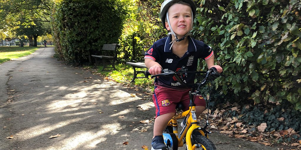 A infant boy, Sam, cycling on his yellow bike through the park on a sunny day