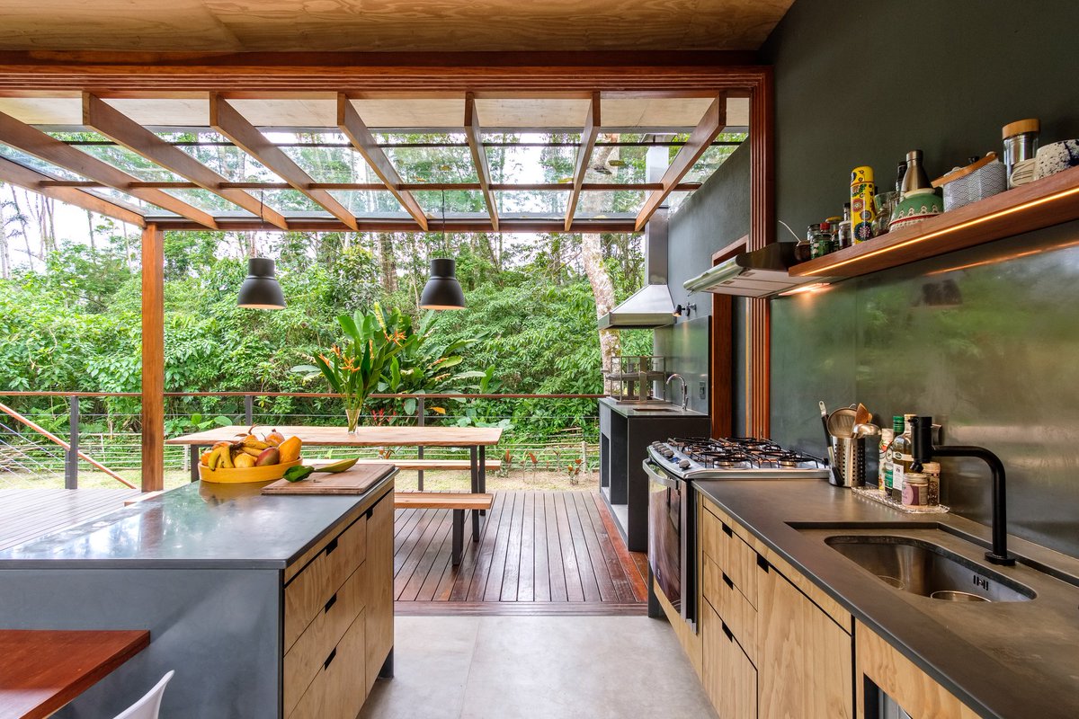 Kitchen and dining space connected to a raised deck with a pergola opening up to the lush tropical vegetation of Ubatuba, São Paulo, Brazil