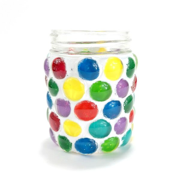 Calling all mason jar craft lovers! This glass décor piece casts a vibrant glow through colored glass gems while holding a votive candle securely inside. Stop by for the tutorial! #MasonJarCrafts #DollarStoreCrafts #Mosaic #GlassGems #VotiveHolder bit.ly/31u7YW7