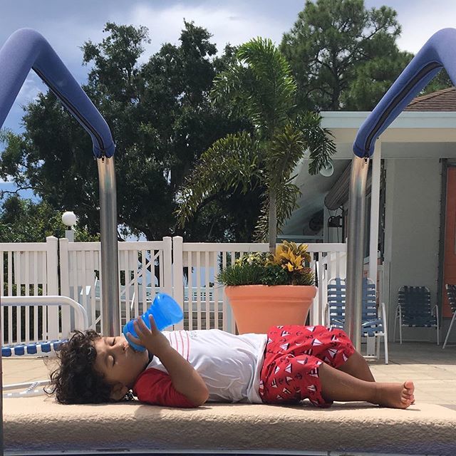 A boy drinking a bottle by a pool.