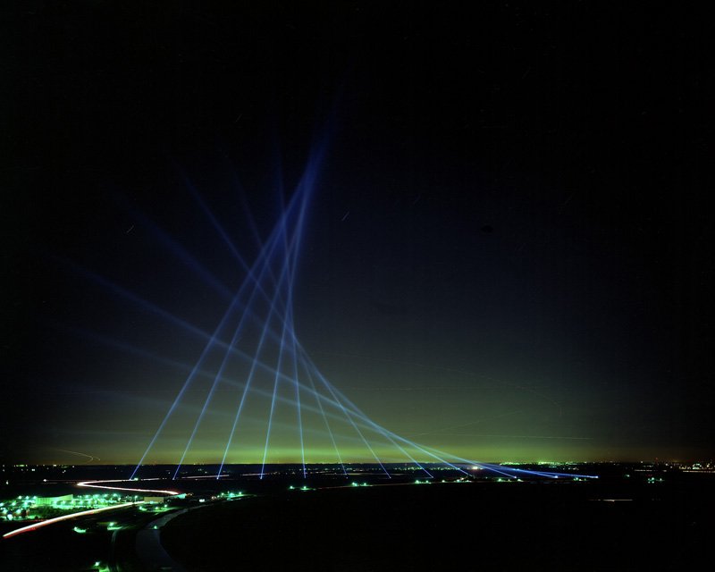 A parabola formed in the sky by about 12 beams of blue light.