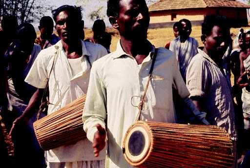 TUMDAK (MADAL)drum made of wood or burnt clay shells & animal skin. always made in pairs, tuned together in same pitch. left side produces a deeper sound than right one. worn around shoulders with a Kandhach (leather strap) played accompanying Santhal Dance.