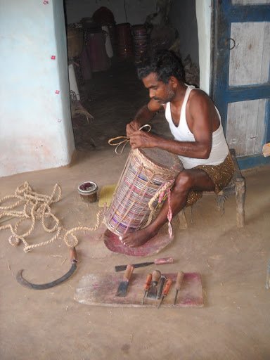 TUMDAK (MADAL)drum made of wood or burnt clay shells & animal skin. always made in pairs, tuned together in same pitch. left side produces a deeper sound than right one. worn around shoulders with a Kandhach (leather strap) played accompanying Santhal Dance.